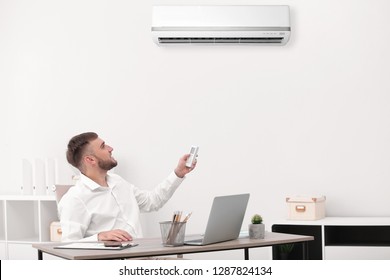 Young Businessman Turning On Air Conditioner In Office