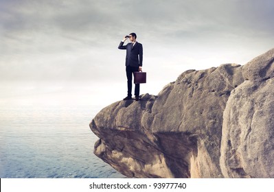 Young businessman using binoculars from a rock over the sea - Powered by Shutterstock