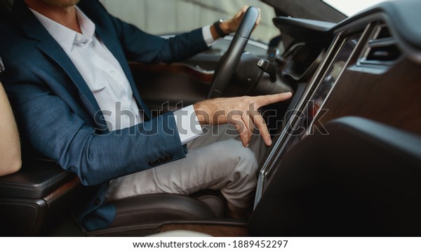 Young businessman using car computer while sitting in\
driver seat inside luxury car, widescreen. Technology and\
application in electric\
car