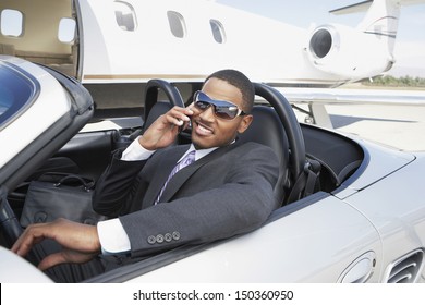 Young businessman using cell phone in convertible near private jet - Powered by Shutterstock