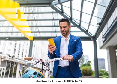 Young Businessman Using Cellphone While Walking Holding His Bike. Latino Business Man Using Mobile Phone Outdoors. Business Concept.