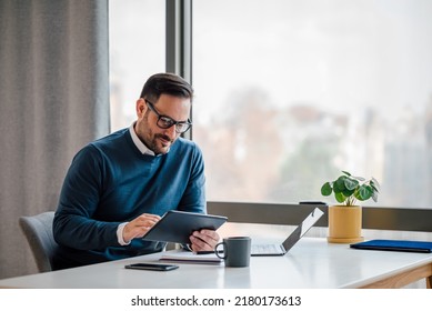 Young businessman using digital tablet while working on laptop in business office. Male professional with wireless computer at desk. He is sitting by window in office. - Shutterstock ID 2180173613