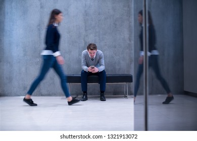 Young Businessman Using Smart Phone While Sitting On The Bench At Busy Office Lobby During A Break