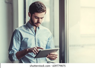 Young businessman using tablet, standing near the window