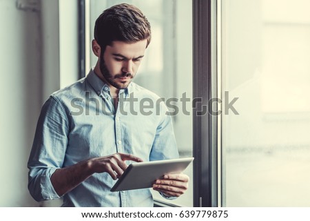 Young businessman using tablet, standing near the window
