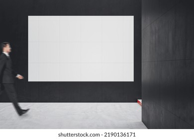 Young Businessman Walking In Creative Dark Concrete Tile Interior With Stairs And Mock Up Poster On Wall. School Hallway And Corridor Concept