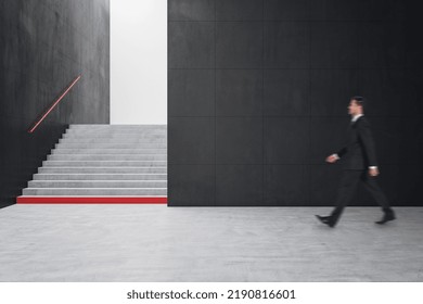 Young Businessman Walking In Creative Dark Concrete Tile Interior With Stairs And Mock Up Place On Wall. School Hallway And Corridor Concept