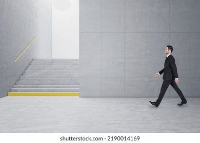 Young Businessman Walking In Creative Light Concrete Tile Interior With Stairs And Mock Up Place On Wall. School Hallway And Corridor Concept