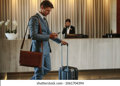 Young businessman walking in hotel lobby and using mobile phone. Business traveler arriving at his hotel.