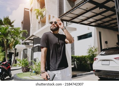 Young Businessman Walking Out Of His Modern Home With Garage And Car