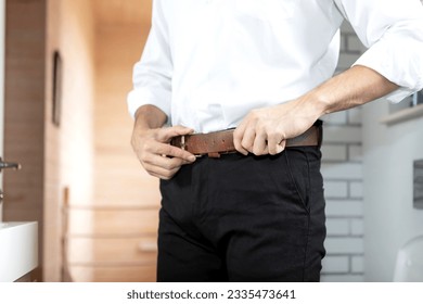 Young businessman wearing pant belt in the room, close-up photo. Preparation for new busy day