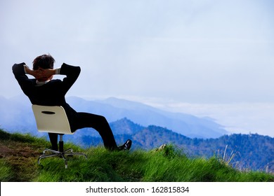 Young businessman who sits on a chair at the top of the mountain and looks into the sky - Powered by Shutterstock