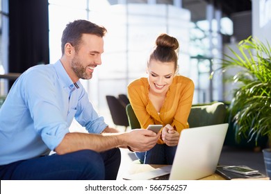 Young Businessman And Woman Sat Working Together In Office With Laptop And Mobile