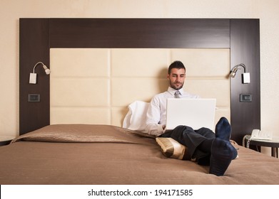 Young Businessman Working With Computer Sit On Bed In Hotel Room. 