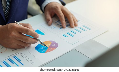 A young businessman working at home holding a pen pointing at a document graph on the desk