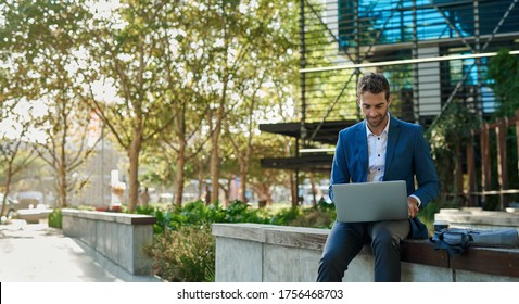 Young businessman working online with a laptop while sitting on a bench outside of his office building - Powered by Shutterstock