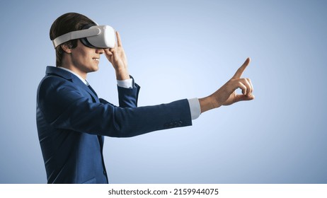 Young Businessman Working In Virtual Reality Office In VR Glasses, Presses His Finger Virtual Interface On Abstract Light Blue Backdrop. Innovate And Future Technology Concept, Close Up