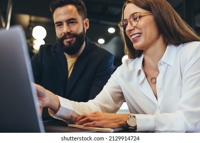 Young businesspeople smiling while using a laptop in an office. Happy young entrepreneurs collaborating in a modern workspace. Two successful businesspeople sitting together at a table. - Shutterstock ID 2129914724