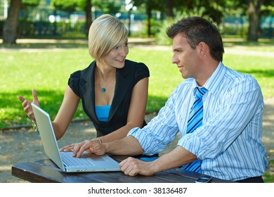 Young businesspeople using laptop computer outdoor, smiling.