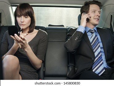 Young Businesswoman Applying Lip Gloss And Businessman Using Cell Phone In Car