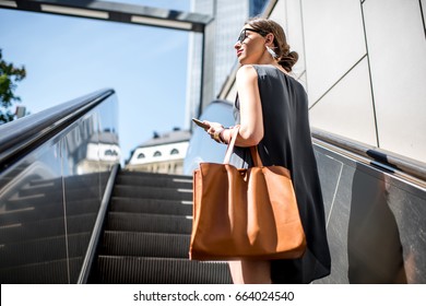 Young businesswoman with bag and phone getting up on the escalator during the business trip in the modern city - Shutterstock ID 664024540
