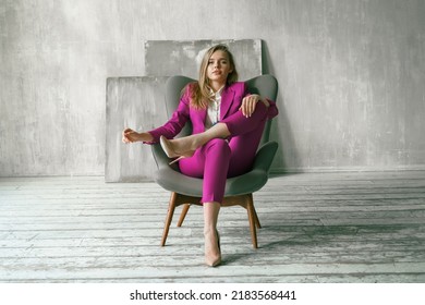 Young businesswoman. Beautiful woman director, head, general manager, ceo in astylish bright business pink, fuchsia color suit at photoshoot in armchair. Business purposeful ambitious girl careerist.
