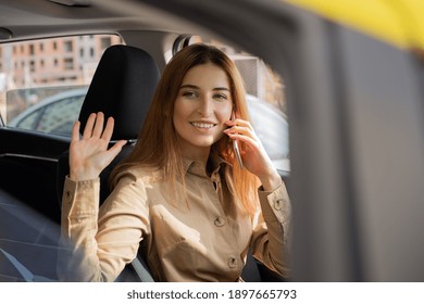 Young Businesswoman Behind The Driver's Seat Talking On The Phone While Stopping And Waving Hello Through The Window