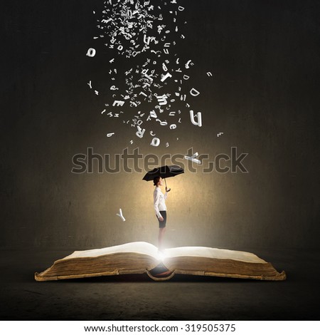 Young businesswoman with black umbrella standing on book