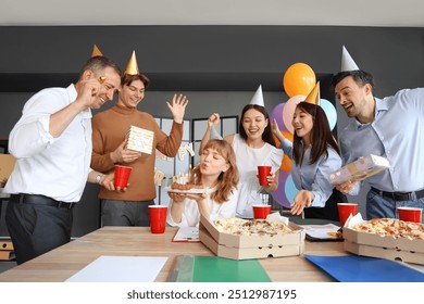 Young businesswoman with cake and her colleagues making wish at birthday party in office - Powered by Shutterstock