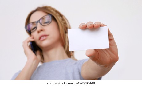 A young businesswoman calling on a mobile phone shows blank visit card in her outstretched hand close-up - Powered by Shutterstock