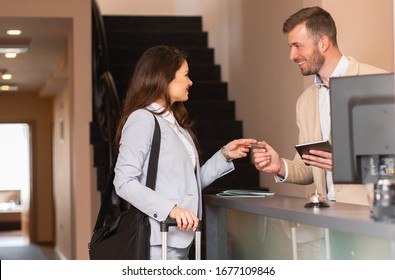 Young businesswoman check-in in hotel, smiling male receptionist behind the hotel counter showing available rooms on tablet.