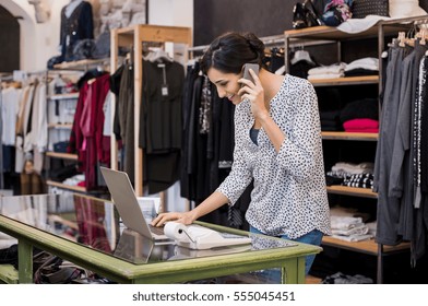 Young Businesswoman Checking Laptop In Her Clothing Store. Young Entrepreneur Using Laptop And Talking On Mobile. Store Manager Woman Checking Important Documents On Laptop. Small Business Concept.