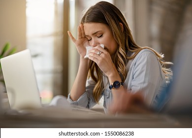 Young businesswoman with clpd and flu virus blowing nose while working in the office. 