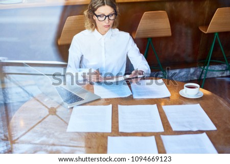 Young businesswoman concentrating on reading texts of new contracts and notifying their main points