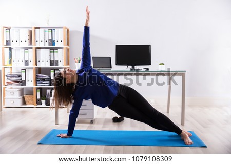 Young Businesswoman Doing Stretching Exercise On Exercise Mat At Workplace