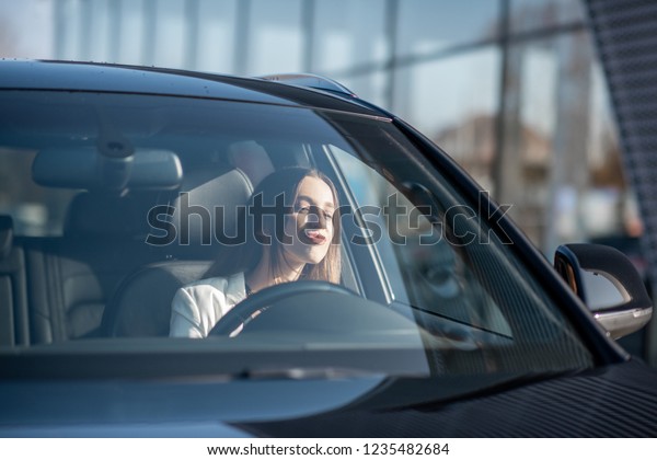 Young businesswoman driving a luxury car,\
view from the outside through the\
windshield