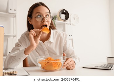 Young businesswoman eating potato chips at table in office - Powered by Shutterstock