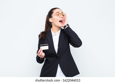 young businesswoman feeling happy, excited and surprised, looking to the side with both hands on face with banknotes with bills