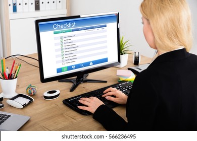 Young Businesswoman Filling Checklist Form On Computer At Wooden Desk