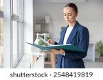 Young businesswoman with folder near window in office