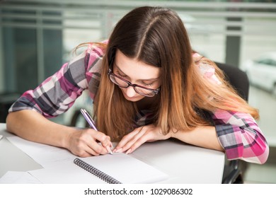 young businesswoman girl with glasses in casual wear sitting at the table carefully look at the documents and write notes in your task