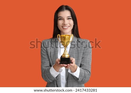 Young businesswoman with gold cup on orange background
