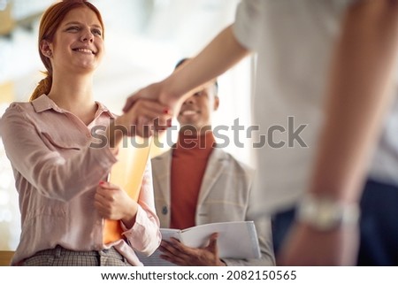 A young businesswoman is handshaking with a colleague she met in a friendly atmosphere in the hallway. Business, people, company