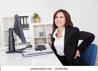 Young Businesswoman Having Back Pain While Sitting At Office Desk