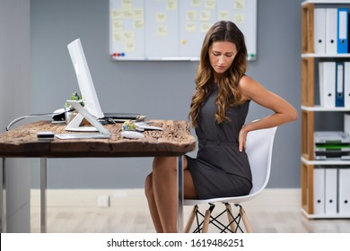 Young Businesswoman Having Back Pain While Sitting At Office Desk