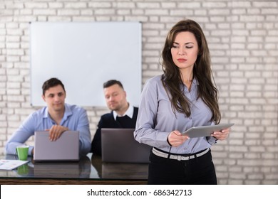 Young Businesswoman Holding Digital Tablet In Front Of Two Businessman In Office