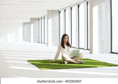 Young businesswoman with laptop sitting on turf in empty office - Powered by Shutterstock