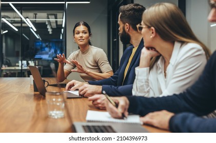 Young businesswoman leading a discussion during a meeting with her colleagues. Group of diverse businesspeople working together in a modern workplace. Business colleagues collaborating on a project. - Shutterstock ID 2104396973
