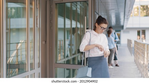 Young Businesswoman Leaving Office Building And Disinfecting Hands With Sanitizer. Female Employee Walking Out Of Business Center Entrance Door Clean Hands With Antiseptic Gel