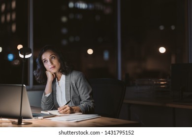 Young businesswoman looking bored and tired while writing notes and using a laptop at her office desk late in the evening - Shutterstock ID 1431795152